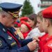 A Russian officer in uniform pinning a badge on a young recruit during an outdoor military ceremony.