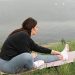 A woman stretches on a yoga mat by a serene lake, embodying relaxation and wellness in nature.
